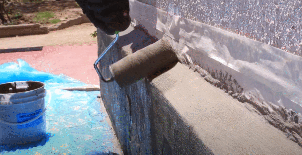 Aplicación de Impercrom Flex con rodillo sobre muro exterior protegido con cinta y lona de seguridad