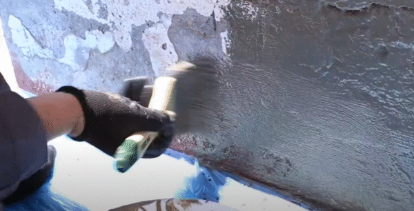 Mano aplicando Impercrom Flex con brocha sobre muro con superficie disgregada y presencia de humedad