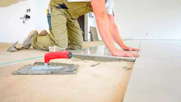 Trabajador instalando porcelanato sobre adhesivo cementoso Weber Doble Acción con llana y alineación manual en piso interior