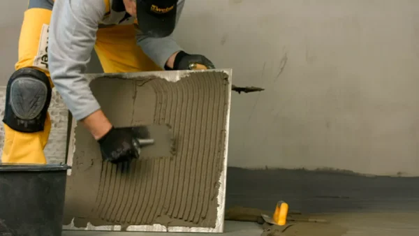 Trabajador aplicando adhesivo Weber Porcelanato Doble Acción con llana sobre el reverso de baldosa grande para instalación en muro interior